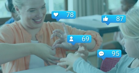 Playing teacher and three kids playing hand game at desks, peach cardigan showing social icons