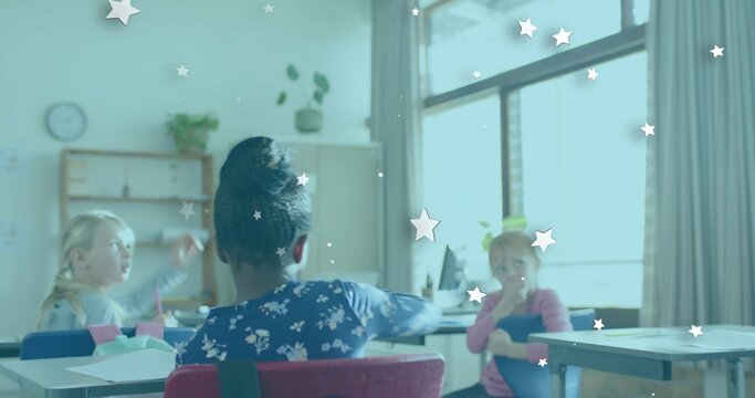 Sitting child with bun wearing dark blue floral top in classroom, blue folder and star stickers