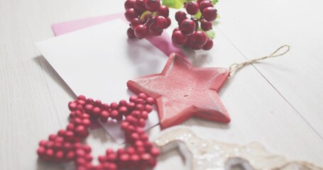 Displaying red star ornament resting on light wood table, with pink card and beaded garland © vectorfusionart