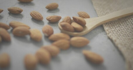 Fototapeta premium Displaying wooden spoon holding whole almonds on gray stone slab, burlap cloth nearby