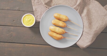 Presenting plate with four skewered corn dogs on dark tabletop, with mustard bowl and linen napkin