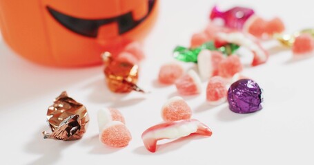 Fototapeta premium Displaying Halloween candies with gummy dentures, gumdrops, jack-o'-lantern bucket on white surface
