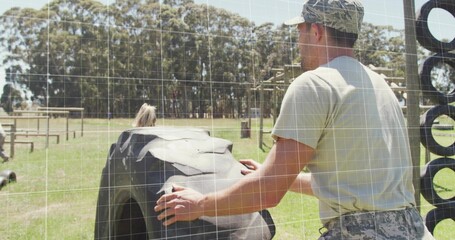 Pushing man wearing camo cap and pants flipping tractor tire on training field, wooden obstacles