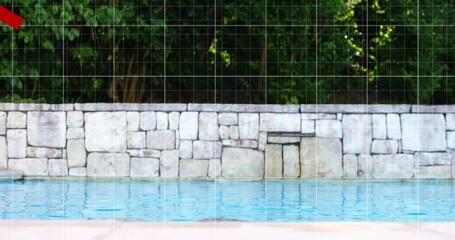 Showing pool water rippling in backyard by stone wall and green treeline, pale deck, red triangle
