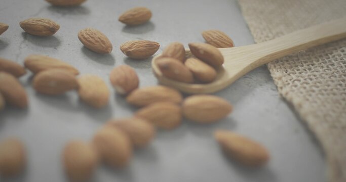 Displaying wooden spoon holding whole almonds on gray stone slab, burlap cloth nearby - Powered by Adobe