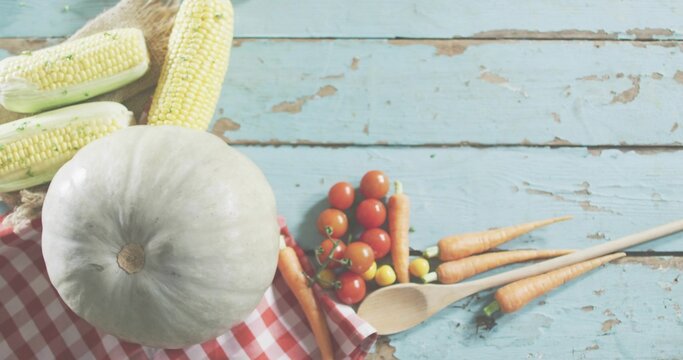 Showing white pumpkin sitting on red-gingham on turquoise tabletop, corn, cherry tomatoes, carrots