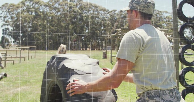 Pushing man wearing camo cap and pants flipping tractor tire on training field, wooden obstacles - Powered by Adobe
