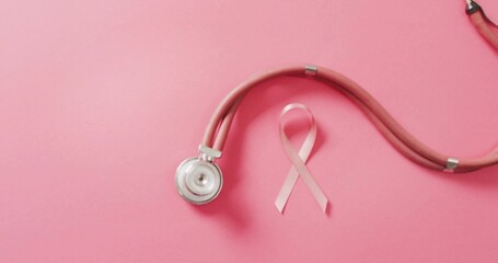 Displaying pink stethoscope and awareness ribbon lying on pastel pink surface, silver chest piece