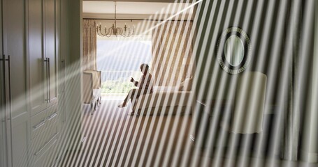 Sitting senior woman wearing dark casual clothes holding mug on bed edge in bedroom, chandelier