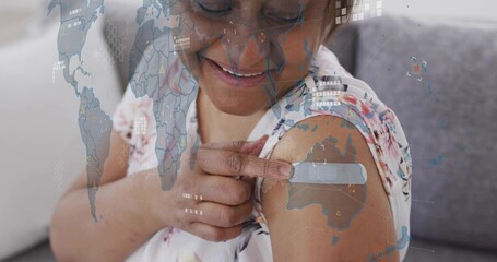 Smiling woman pointing to bandage on arm at home, wearing floral blouse with map overlay