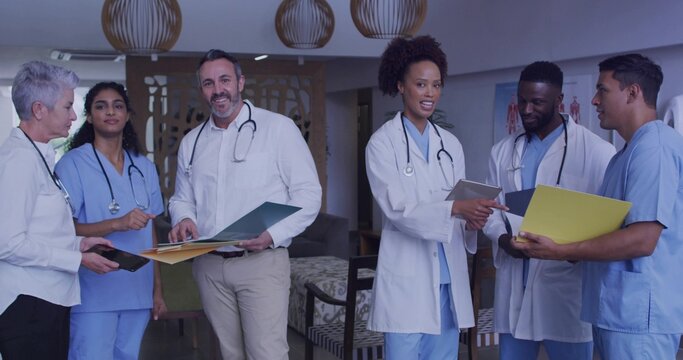 Reviewing charts, six staff in lounge wearing white coats holding folders, tablet, stethoscopes