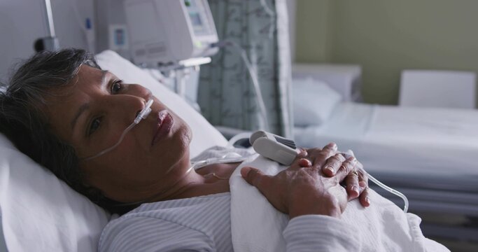 Resting senior woman lying in hospital bed, in striped top with nasal cannula and pulse oximeter