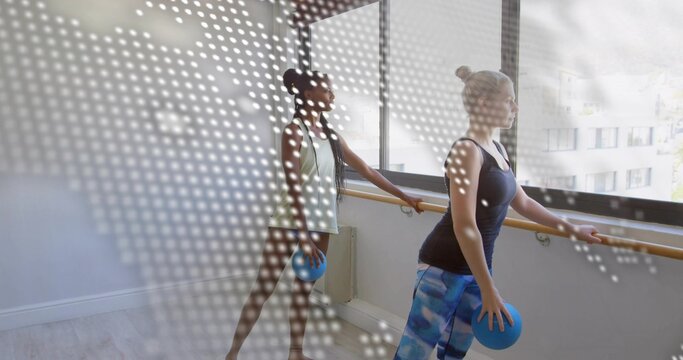 Practicing pair wearing activewear holding blue balls at barre in studio window dots, copy space - Powered by Adobe