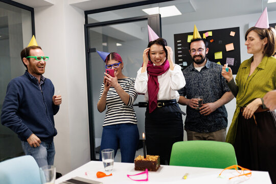 Celebrating success with colleagues at a business gathering in an office setting during an afternoon event with fun party hats and a cake
