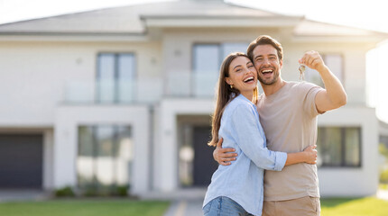 Happy couple celebrating their new home with keys in hand in bright daylight outside a modern house