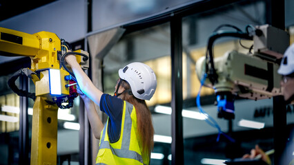 Two female robotics engineers in an R and D lab test an artificial intelligence cobot. They are...