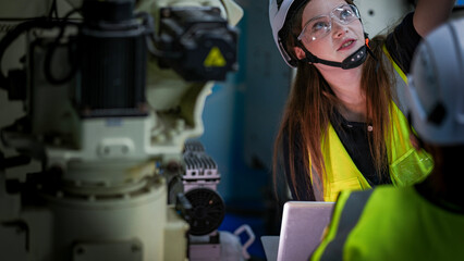 Two female robotics engineers in an R and D lab program an artificial intelligence cobot. They are testing the robotic system hardware and programming using a tablet.