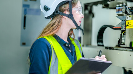 A female robotics engineer in an R and D lab performs diagnostics on an AI system. She is auditing the robotic hardware, wiring, and control panel data.