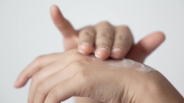 Close-up of hands applying white moisturizing cream to the skin