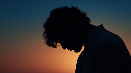 Silhouette of a young man with curly hair at sunset looking down orange sky