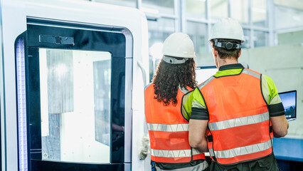 Two engineers use a laptop to program an industrial 5-axis CNC machine. They are programming an AI-driven system for high-precision component manufacturing.