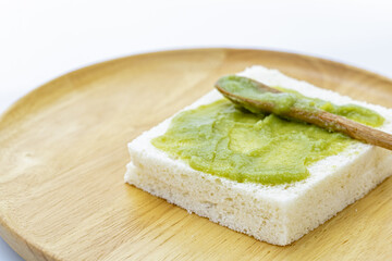 A close-up of a thick slice of white bread with Pandan Custard evenly applied on top, placed on a round wooden plate with a small