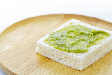 A single slice of white bread with a spread of Pandan Custard is placed on a round wooden plate, showcasing simple and natural