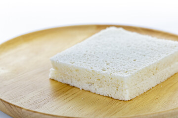 Close-up image of a square slice of white bread on a wooden plate showing soft, porous texture in a simple setting
