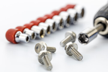 Close-up of silver metal screws with a socket wrench attachment and a row of socket bits with red holders on a white background