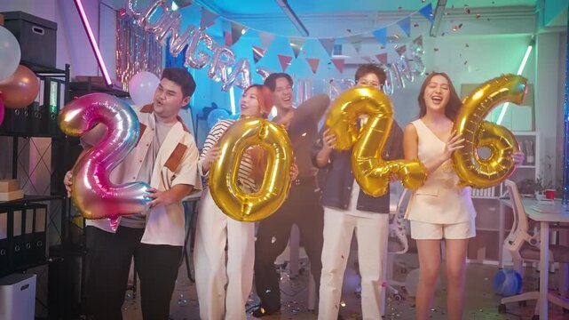 Asian business team celebrating New Year 2026 or major milestone achievement in office party,holding large 2026 foil number balloons and confetti falling.Concept of corporate success,festive teamwork 