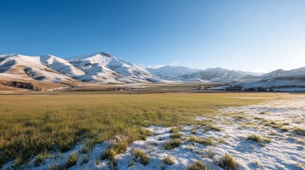 Fototapeta premium Snow-capped mountains and green fields under a clear blue sky in winter landscape