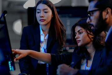 A diverse team of three professionals, one man and two women, collaborates closely around a computer screen, analyzing data and discussing project details in a modern tech office.