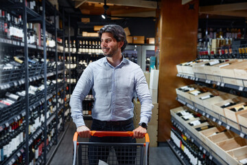Fototapeta premium A man is pushing a shopping cart in a wine store browsing