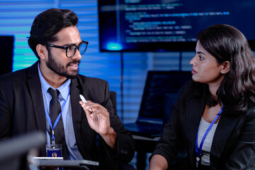 Focused late night strategy session. Male manager with glasses gestures explaining complex points to attentive female colleague in modern high tech command center office.