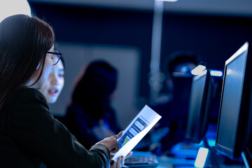 Late night project crunch. Diverse team collaborates intensely focused female professional points critical chart data colleague listens modern tech hub deadline approaching fast.