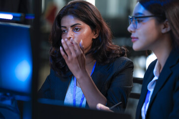 Peak concentration unlocked. Two diverse female professionals collaborate intensely reviewing critical data screen reflects shared focus modern tech hub late night project synergy drives results now.