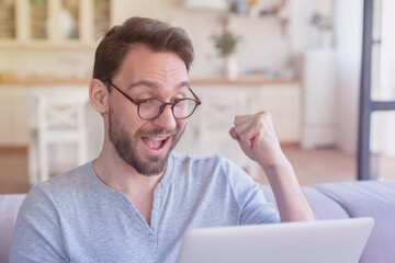 Excited young caucasian man businessman freelancer entrepreneur investor trader using laptop with positive emotions, lottery winner and success, searching web, online learning, home office.
