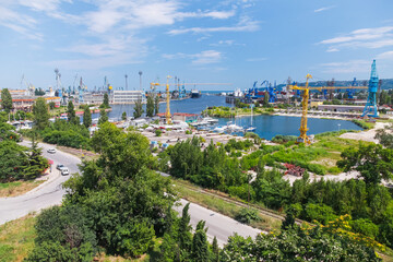 Aerial view of a seaport featuring cranes, docked boats, and lush greenery