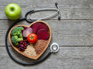 Heart health and nutrition concept with stethoscope and fresh vegetables, fruits, and grains on a rustic wood table.