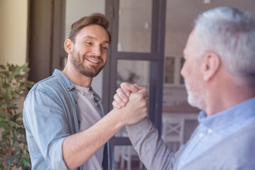 Old elderly senior father together with his young adult son shaking hands as old friends together at home showing support and love. Happy father`s day!