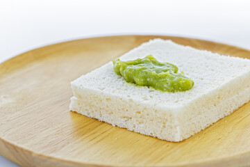 A close-up of a thick slice of white bread with a Pandan Custard placed on top, presented on a round wooden plate against a clean
