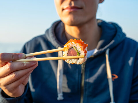 Man holding sushi roll with chopsticks, close-up view.