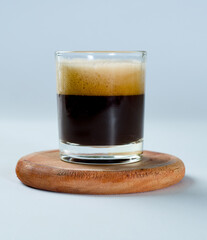 a 60 ml glass of espresso standing on a glass tray made of wood