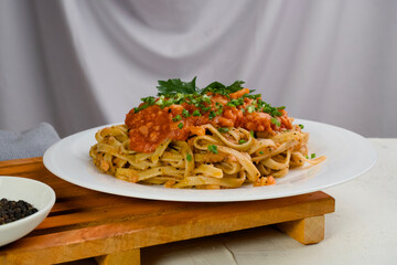 A plate of pasta noodles topped with tomato sauce mixed with meat, cheese, spices, onions and lettuce leaves stands on a wooden tray.
