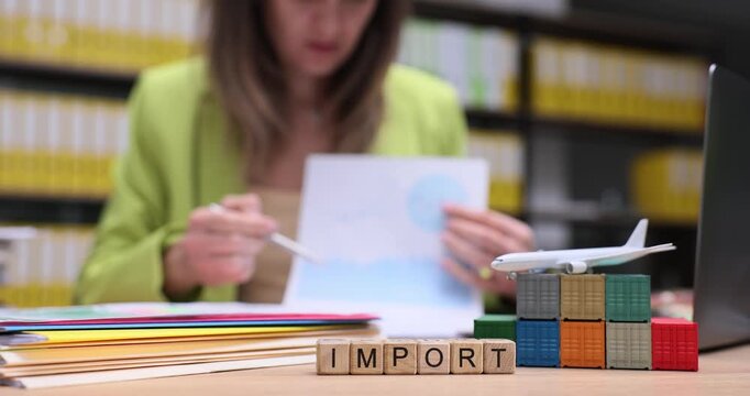 Wooden blocks spell word Import on office desk by toy containers. Businesswoman reads document checking paperwork for international shipping process