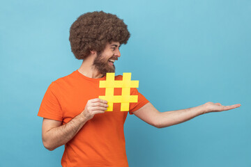 Man holding hashtag in his hand with toothy smile on face, website search, presenting copy space.