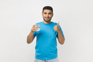 Positive man holding glass with water, recommend to drink at fresh clean water, showing thumb up.