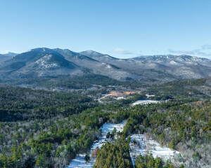 Panoramic winter view of the Adirondack Mountains in New York with forested valleys, snow patches, and clear blue sky.