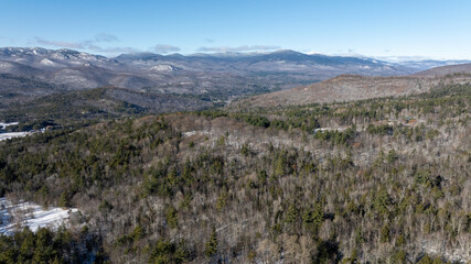 Panoramic winter view of the Adirondack Mountains in New York with forested valleys, snow patches, and clear blue sky.