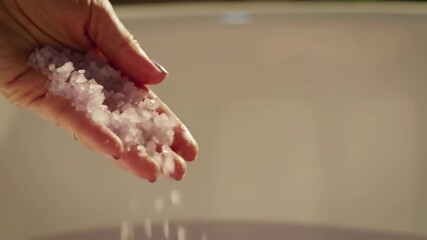 A close-up captures the meticulous gesture of a hand releasing coarse salt, embodying both the art of culinary seasoning and the serenity of a spa wellness ritual